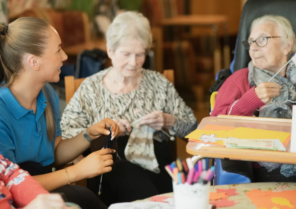 Caregiver assisting senior women with knitting